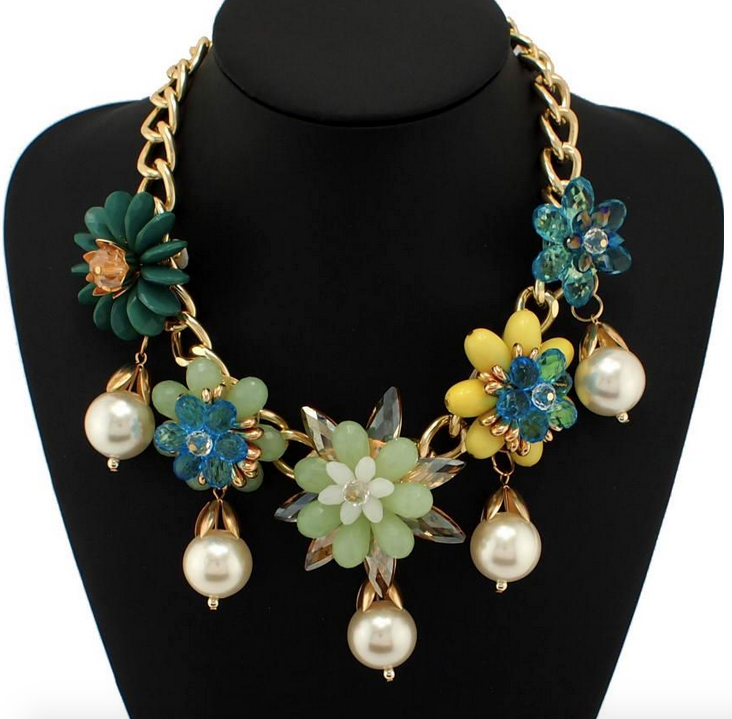Close-up of a gold chunky chain necklace featuring green, blue, and yellow resin flowers with crystal centers and hanging pearl drops on a black mannequin